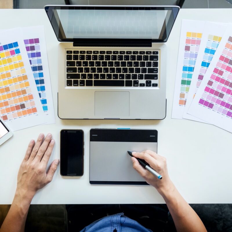 Top view of a young graphic designer working on a desktop computer and using some color swatches, top view.